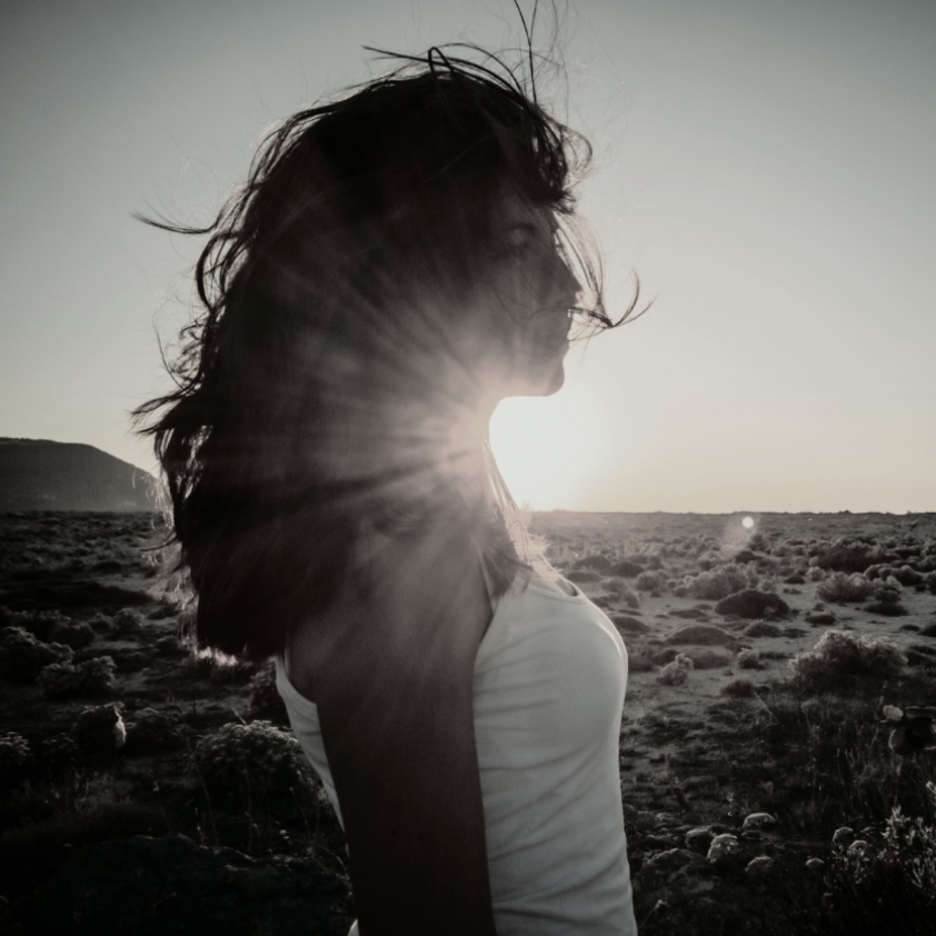 Person standing in a field with a sunburst effect during sunset