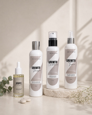 The Aotea Roots Ritual Set: the Growth pre-wash oil bottle, the shampoo and conditioner bottles and the tonic bottle arranged in a row on a pale surface.